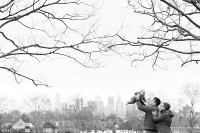 Parents hold up a baby with London in the background.