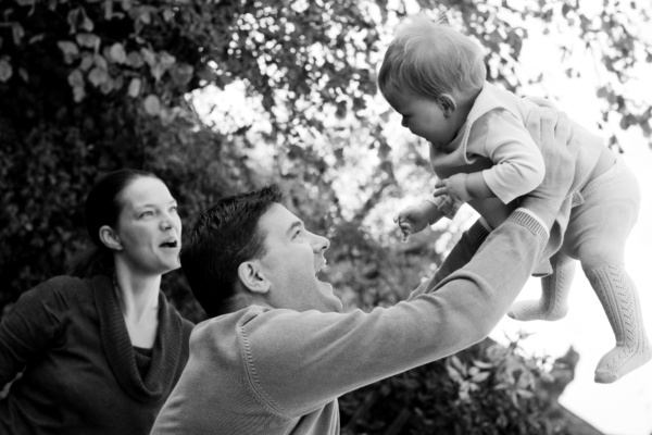 Parents hold up a baby in the air outdoors.