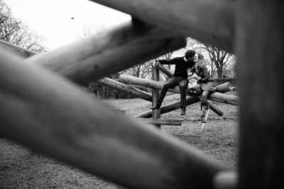 Parents kiss in a playground, framed by wooden playground equipment.