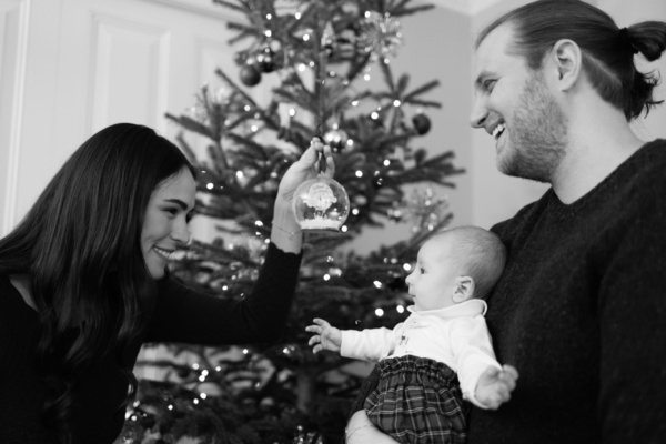 Parents laugh with a baby at Christmas, in front of their tree.