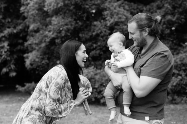 Parents make their baby giggle against a background of trees.