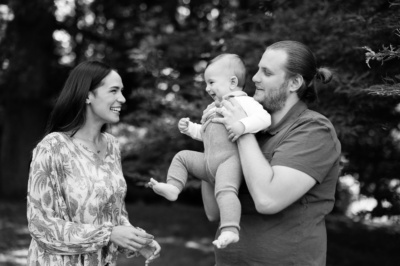 Parents play with their baby near trees.