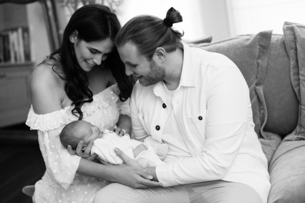 Parents sit on a sofa with their newborn baby.