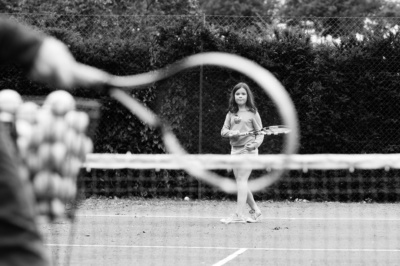 A racquet frames a child playing tennis.