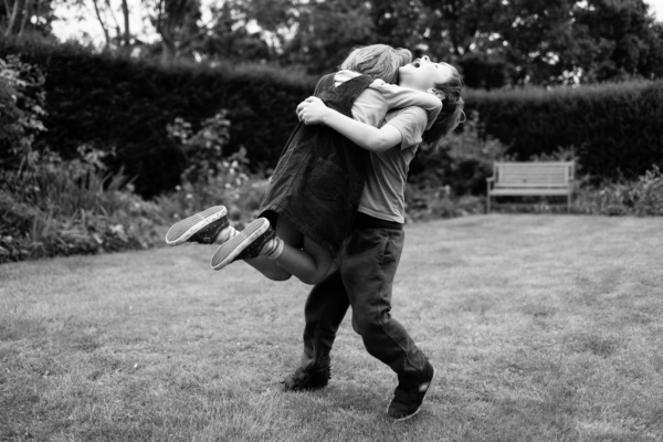 Siblings hug each other in a garden.