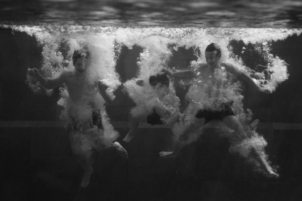 Siblings jump into a pool, creating bubbles.