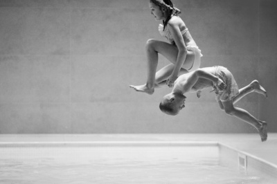 A brother and sister jump into a pool.