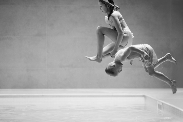 A brother and sister jump into a pool.