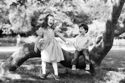 Siblings play near a tree branch.