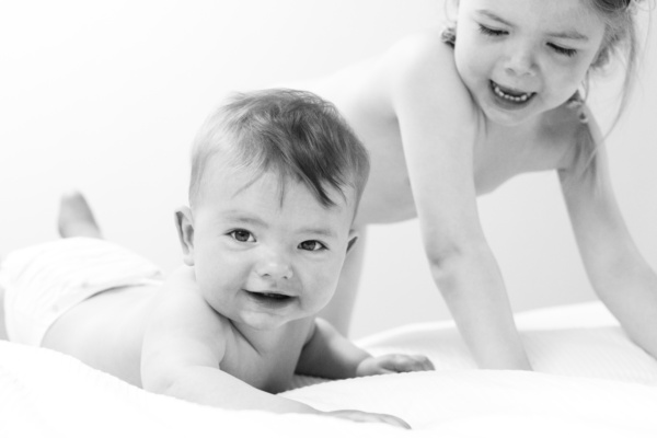 Siblings play on a bed together.