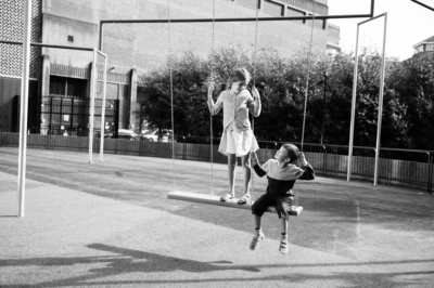 Siblings play on swings in the sunshine.