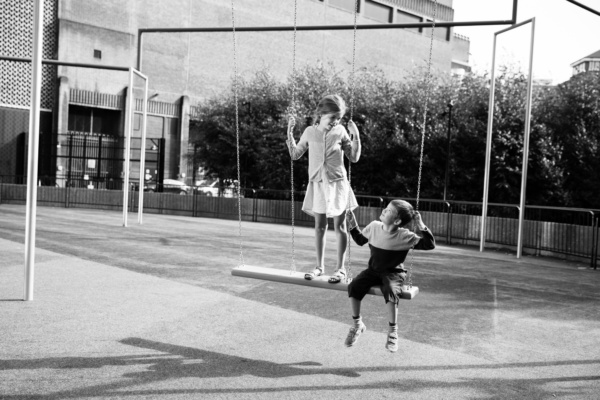 Siblings play on swings in the sunshine.