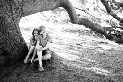 Siblings sit under a tree in a black and white portrait.