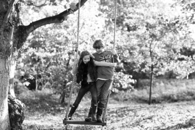 Siblings swing together on a rope and wooden swing.