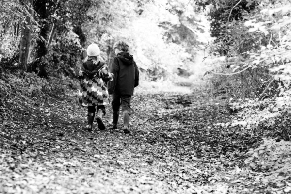 Siblings walk down a woodland path.