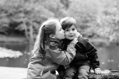 A sister kisses her brother on the cheek with a lake in the background.