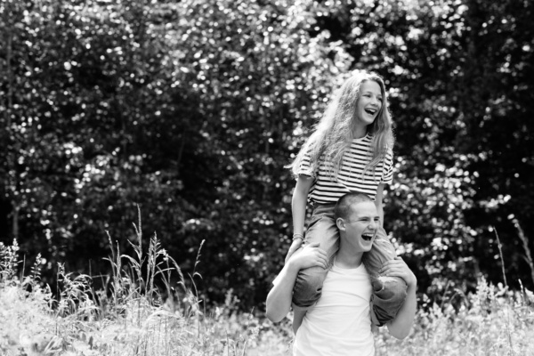 Sister sits on brother's shoulder in field.