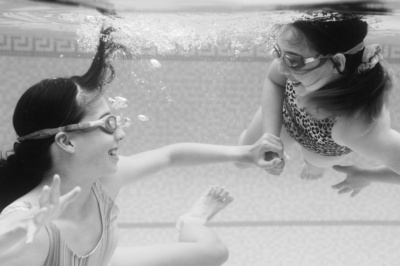 Sisters hold hands underwater.