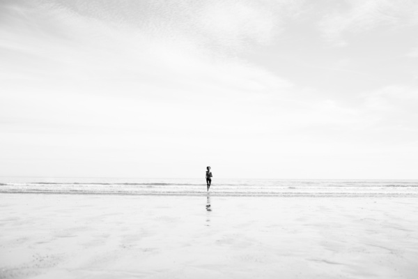 A solo child runs on a deserted beach.