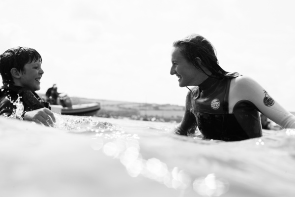 A son and mother play in waves together.