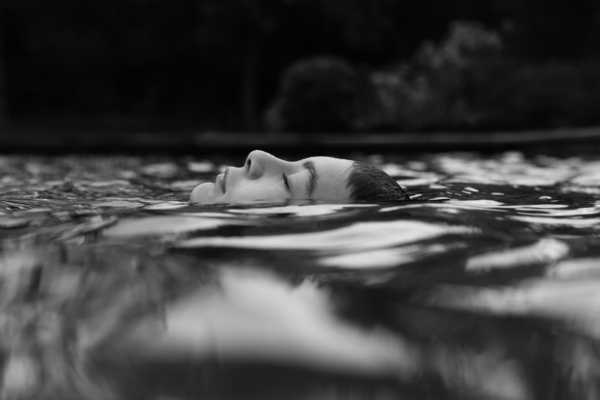 A teenager floats in a pond with their head above water.