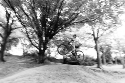 A teenager jumps their trail bike over a small hill.