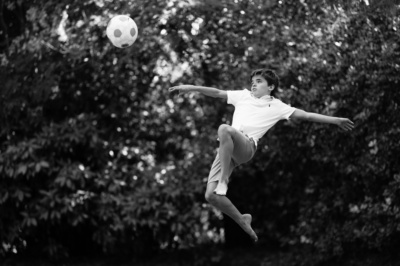 A teen leaps into the air to kick a soccer ball.