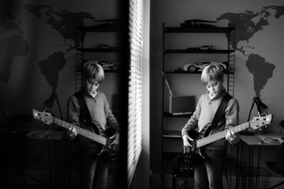 A teenage boy plays the guitar in his room, with a reflection in the mirror.