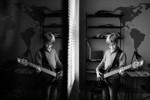 A teenage boy plays the guitar in his room, with a reflection in the mirror.