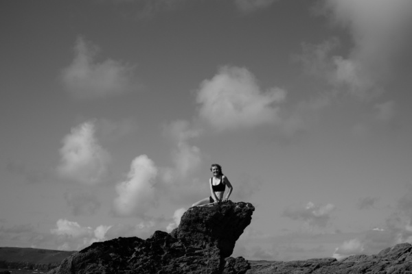 A teen sits on a rock, against a cloudy sky.