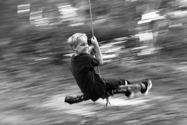 A teen swings through woods on a rustic swing.