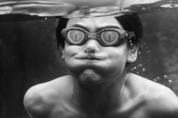 Teen wearing goggles holds his breath underwater.