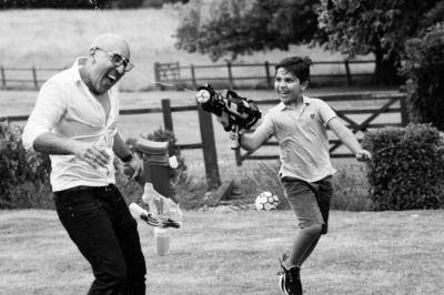 A teenage boy squirts his father with water while they run through a field.