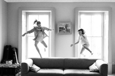 Teenage siblings leap in the air near sofa.