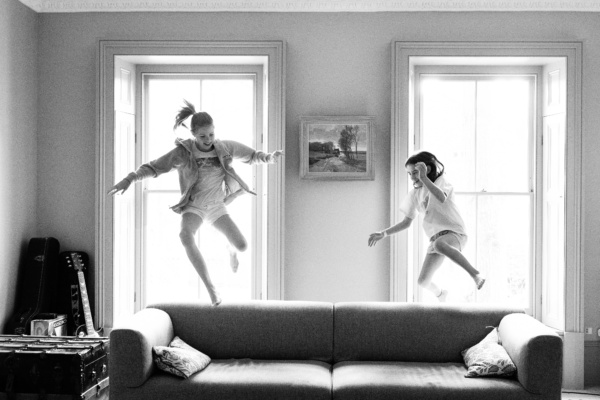 Teenage siblings leap in the air near sofa.