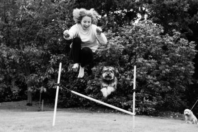 A teenager and her dog leap over a jump.