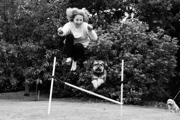 A teenager and her dog leap over a jump.