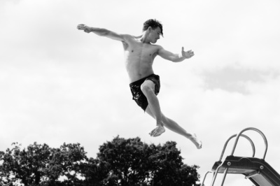 A teenager leaps off a diving board into a pool.