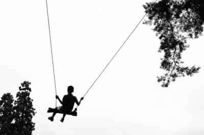 A teenager on a large swing in the trees.