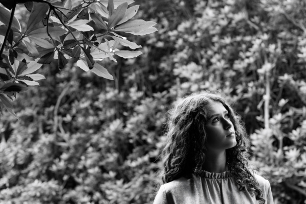 A portrait of a teenager looking skyward against a lush background.