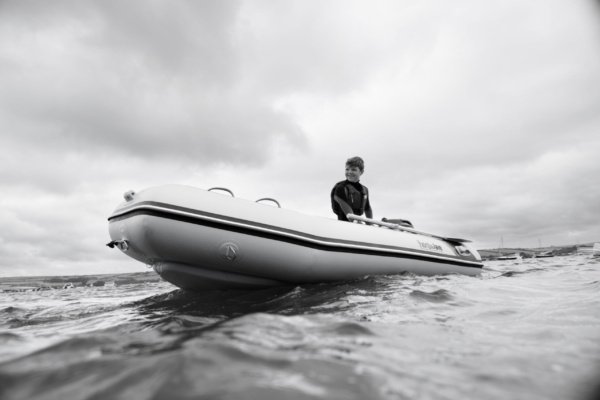 A teenager skippers an inflatable dinghy across the sea in Cornwall.