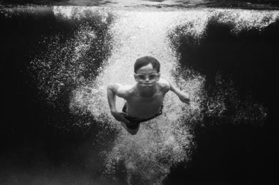 A teenager swims through underwater bubbles.