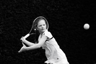 A teenage girl swings her tennis racket at an airborne ball.