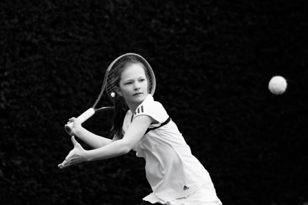 A teenage girl swings her tennis racket at an airborne ball.