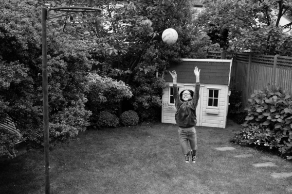 A child jumps with a basketball with a wendy house in the background.