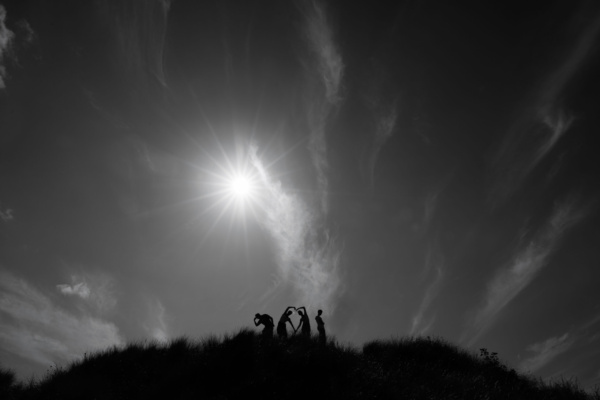 Teenagers stand on a sand dune, forming a silhouette against the sky.