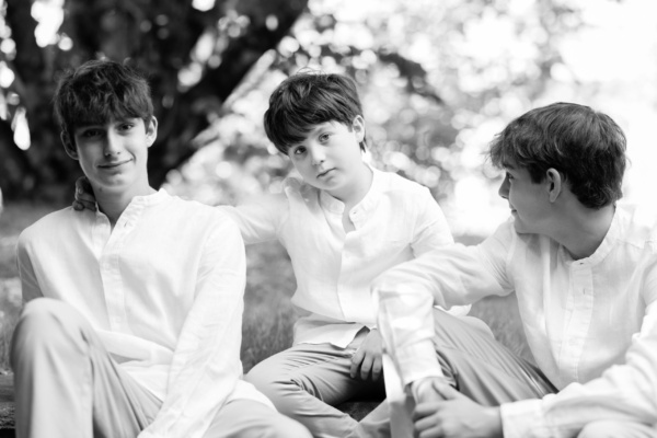 Three teenage brothers wearing white shirts in a relaxed black and white portrait.