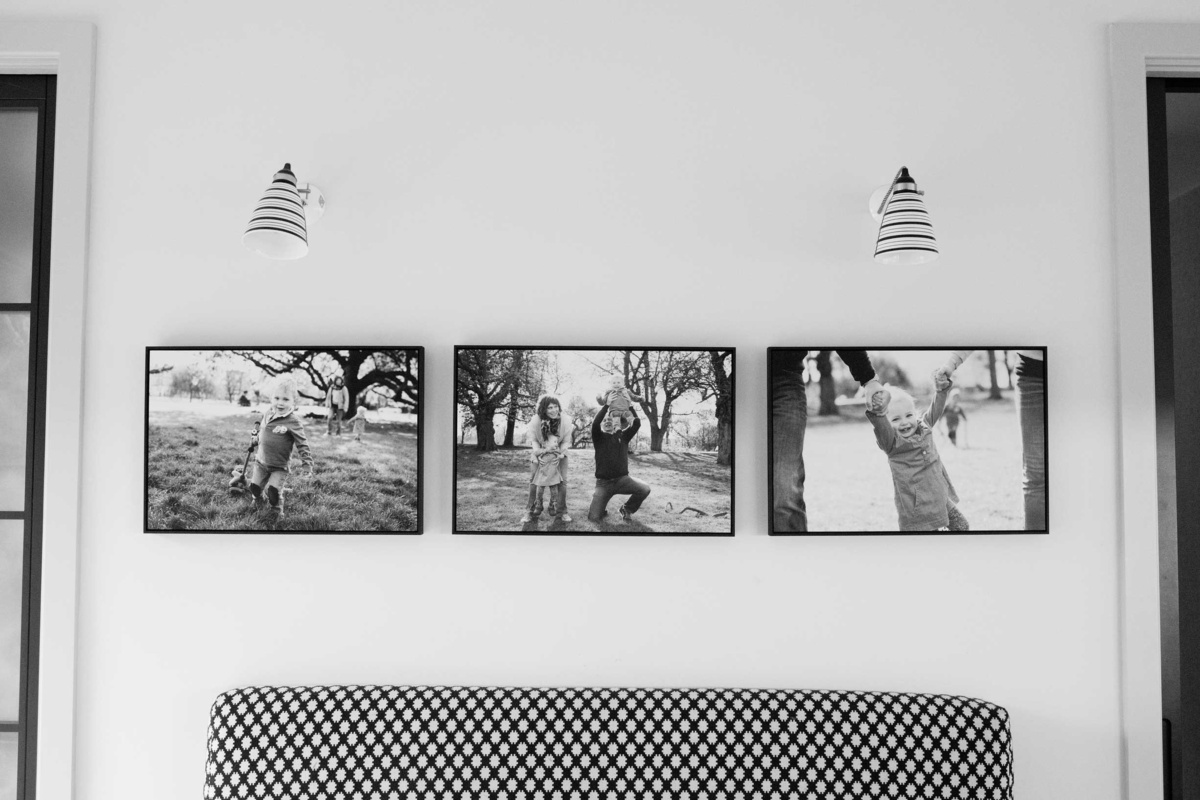 Three tray frames displaying family portraits sit over a small sofa in a family home.