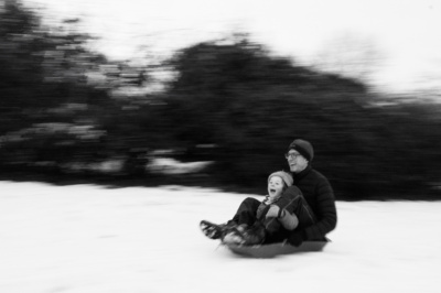 A boy and a man toboggan in the snow.