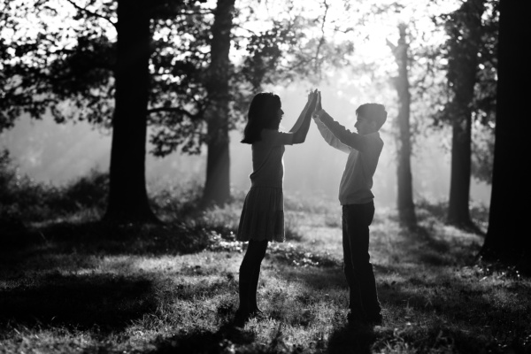 Two teenagers make an arch together in woods.